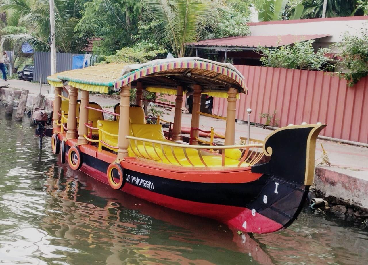 Red and black Alleppey shikara boat with yellow cushioned seats moored at a canal-side jetty
